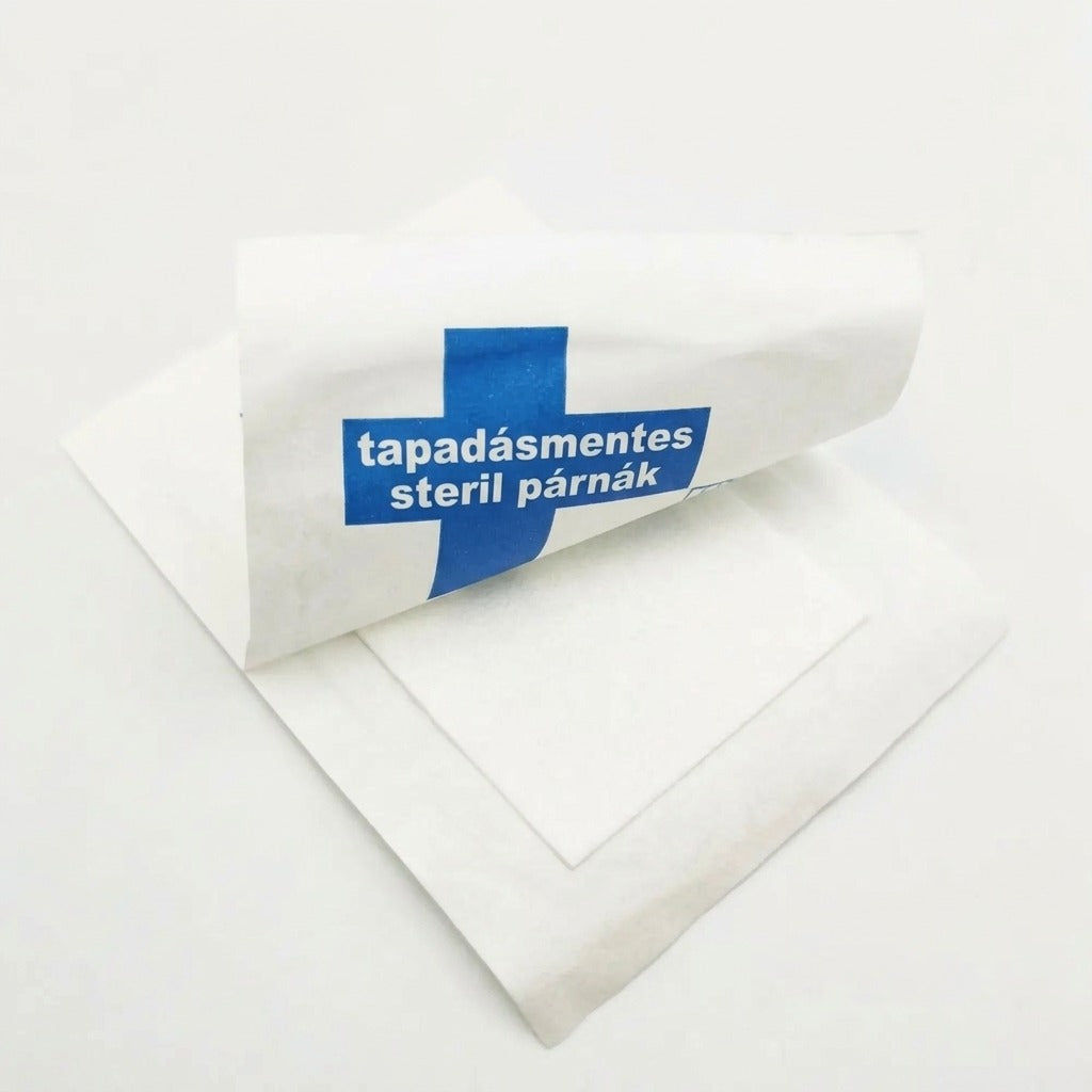 Felbontott csomagolású tapadásmentes steril sebfedő párna fehér háttér előtt.