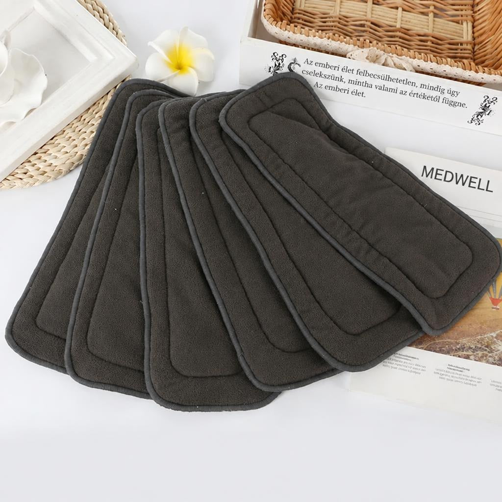 Szürke textil pelenkabetétek Medwell feliratú dekorációval elrendezve egy asztalon.